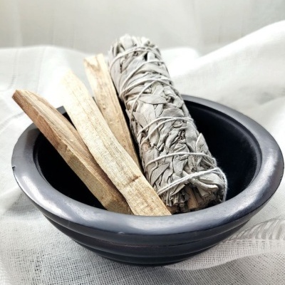 Vaso preto com feixe de ervas e pedaços de madeira sobre tecido branco