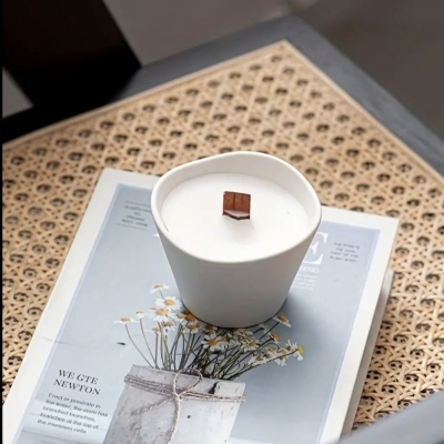 Vela branca em recipiente cerâmico branco com pavio de madeira sobre revista com flores