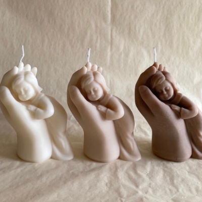 Velas decorativas em forma de mão segurando bebé em várias cores.