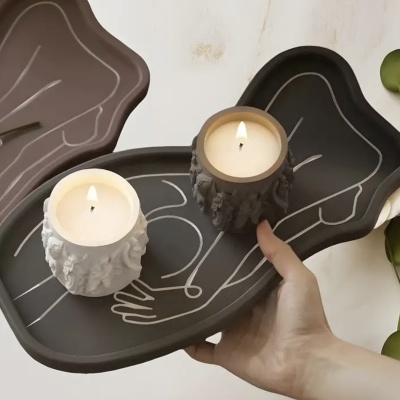 Bandeja cinza com velas aromáticas em recipientes com relevo de faces