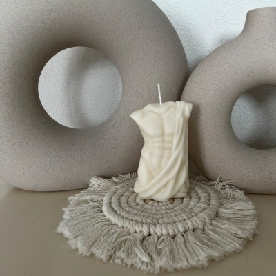 Vela branca em forma de busto masculino sobre suporte têxtil cinzento, com decorações cerâmicas em fundo branco