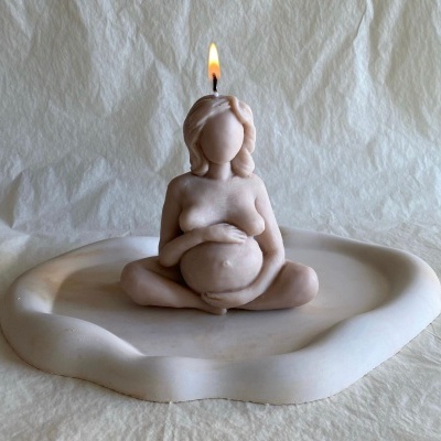 Vela decorativa em forma de mulher grávida sentada com pernas cruzadas em prato branco