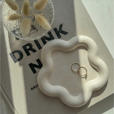 Livro de capa dura com texto preto, prato branco ondulado com anéis dourados e copo transparente com flores secas