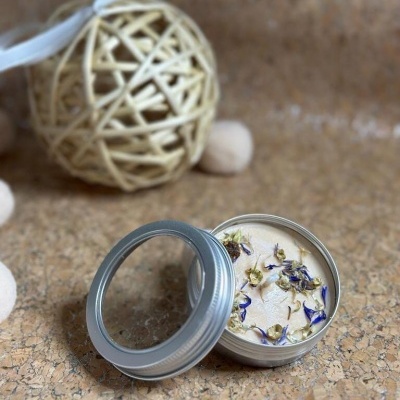 Vela decorativa numa lata metálica com flores secas sobre a cera