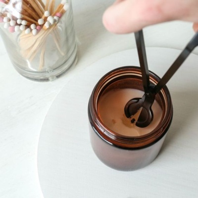 Frasco âmbar com vela cremosa e pinça preta com palito colorido ao lado