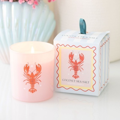 Vela perfumada em copo rosa com desenho de lagosta e caixa ao lado