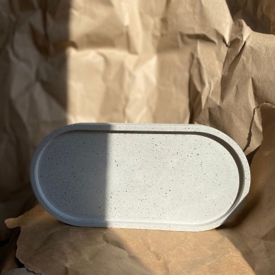 Bandeja oval cinza claro com textura pontilhada sobre papel castanho amassado