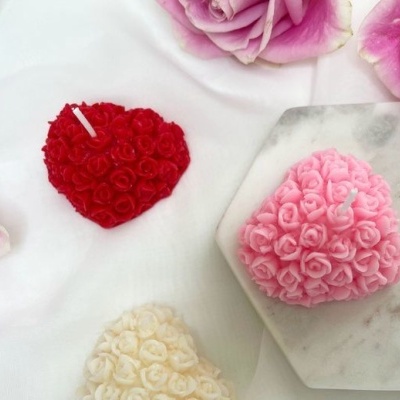 Velas em forma de coração feitas de pequenas rosas nas cores vermelho, cor-de-rosa e creme sobre superfície branca e tábua de mármore.