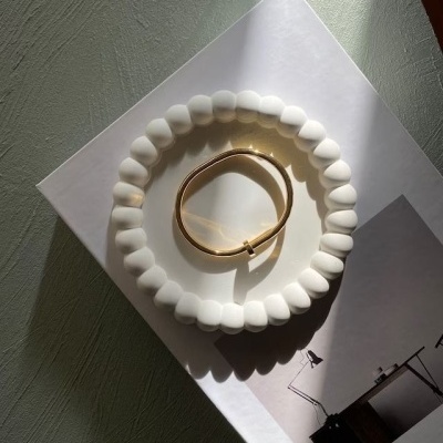 Pulseira branca com contas ao redor de pulseira dourada sobre papel branco iluminado