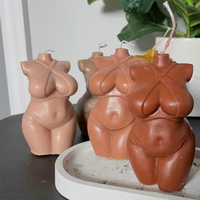 Velas decorativas em forma de corpo feminino em vários tons de pele sobre superfície escura