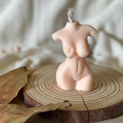 Vela em forma de torso feminino sobre base de madeira com folhas secas