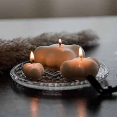 Velas creme formas curvas em prato de vidro, sobre mesa escura, fundo desfocado.