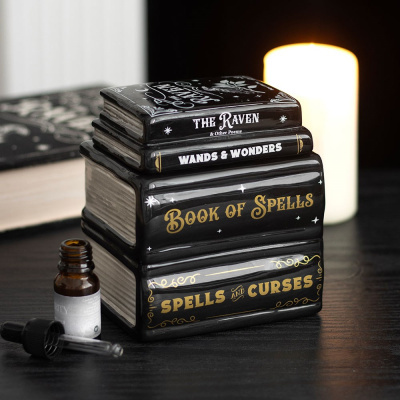 Conjunto de caixas decorativas em forma de livros pretos com títulos em branco e dourado e um frasco com conta-gotas preto sobre uma mesa preta