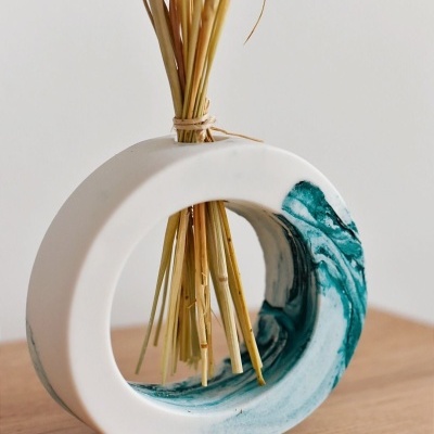 Vaso circular de cerâmica branca com onda azul e ramos secos