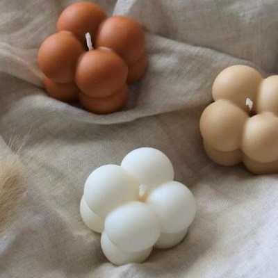 Três velas decorativas em forma de cubos esféricos em tons terra sobre tecido bege