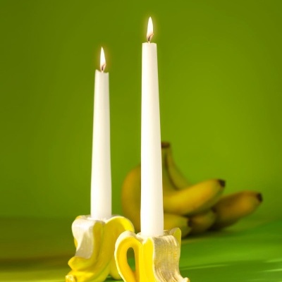 Dois castiçais forma banana com velas acesas em fundo verde com bananas ao fundo