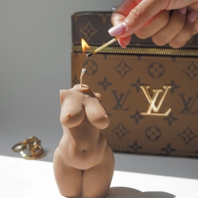 Vela em forma de torso feminino com mala Louis Vuitton ao fundo