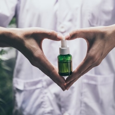 Frasco verde com conta-gotas segurado por mãos que formam um coração
