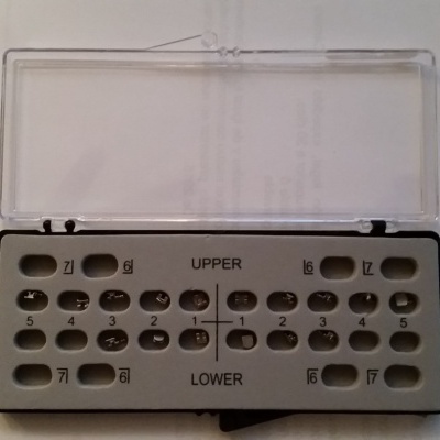 Metal dental bracket holder with transparent lid containing numbered orthodontic brackets