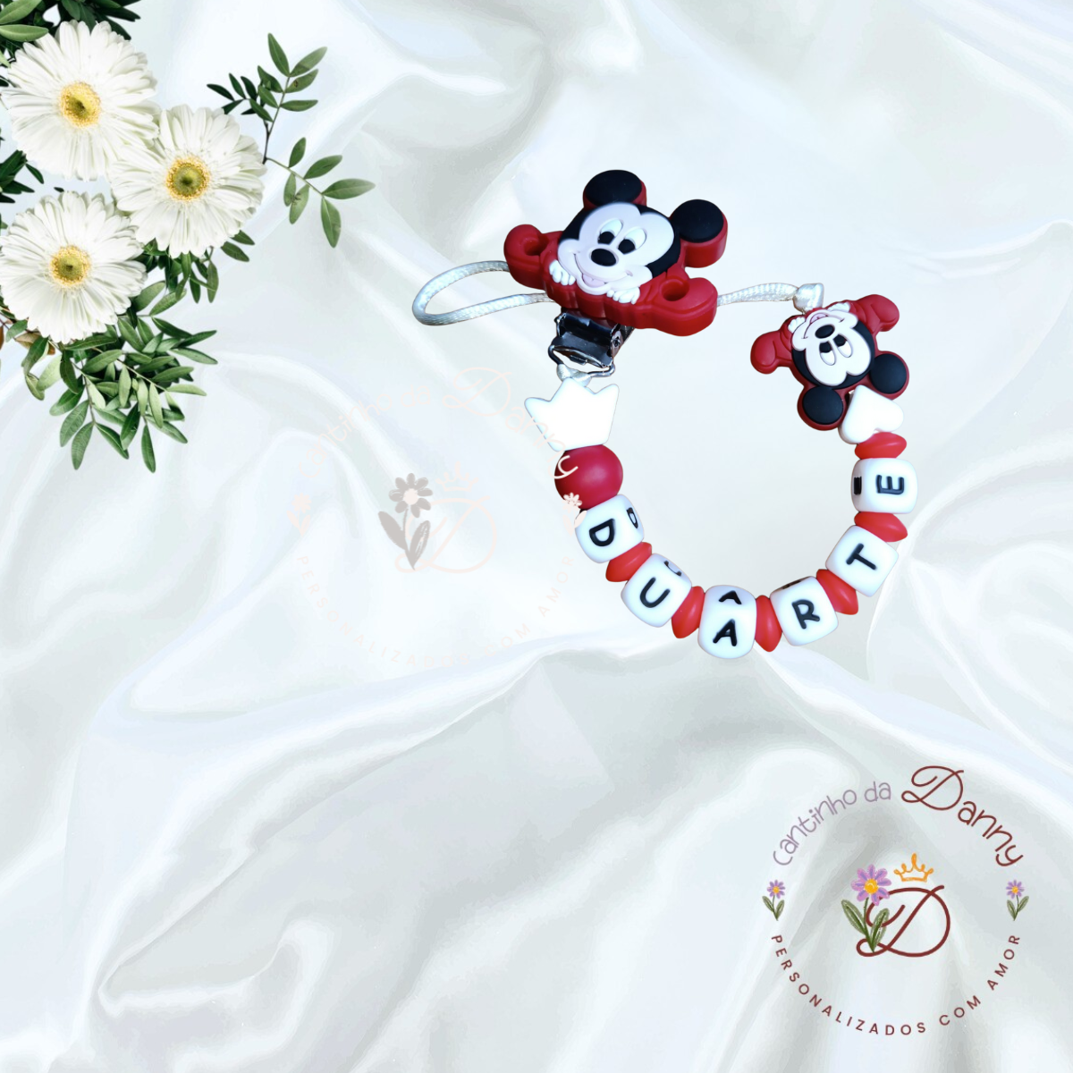 Prendedor de chupeta com personagem Mickey e letras DUARTE sobre tecido branco e flores.