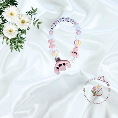 Clipe em silicone com bolas coloridas e nome ARIA ANA, sobre tecido branco com flores