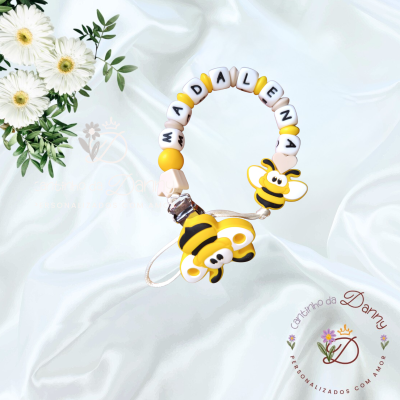 Chupeta personalizada com nome em contas e enfeite de abelha amarelo e preto sobre tecido branco.