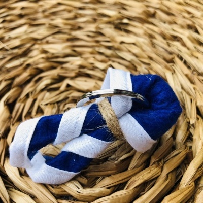 Anel prateado sobre nó de tecido azul e branco em superfície trançada natural castanha