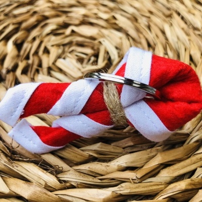 Chaveiro de tecido vermelho e branco listrado com argola metálica em fundo de palha trançada