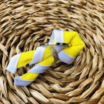 Anel prateado simples sobre feltro amarelo e fita branca em fundo de fibras naturais entrelaçadas