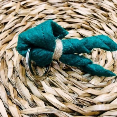 Porta-chaves de tecido verde com nó e argola metálica em fundo de palha trançada