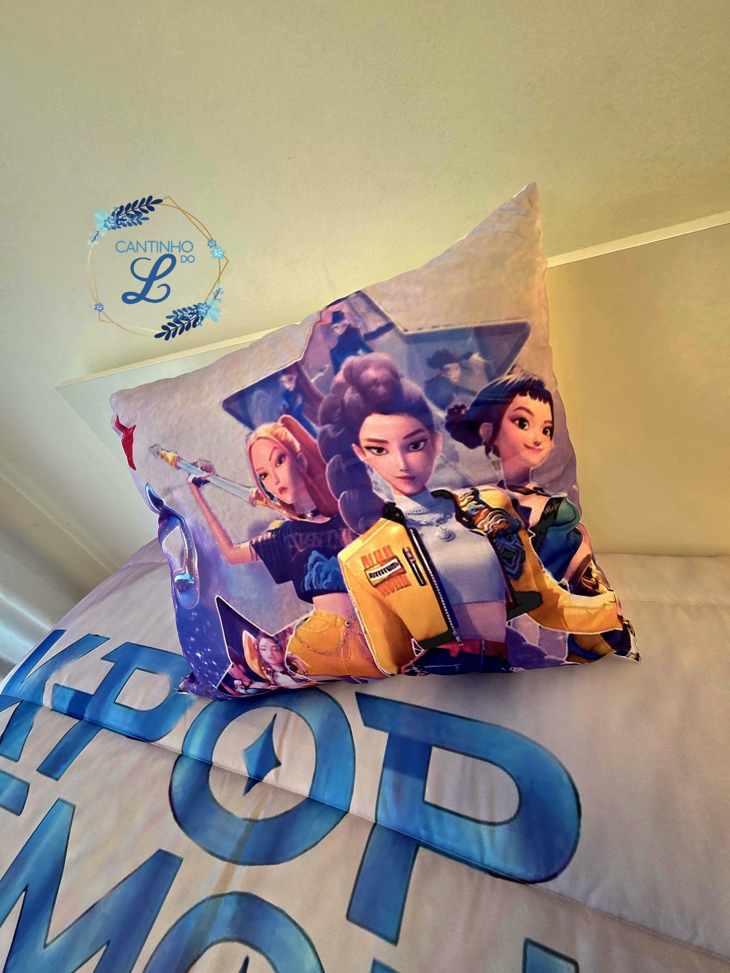 Edredão K-Pop com Estampagem Digital – Roupa de Cama Juvenil Almofada decorativa com personagens animadas femininas sobre cama com roupa de cama branca e azul com texto.