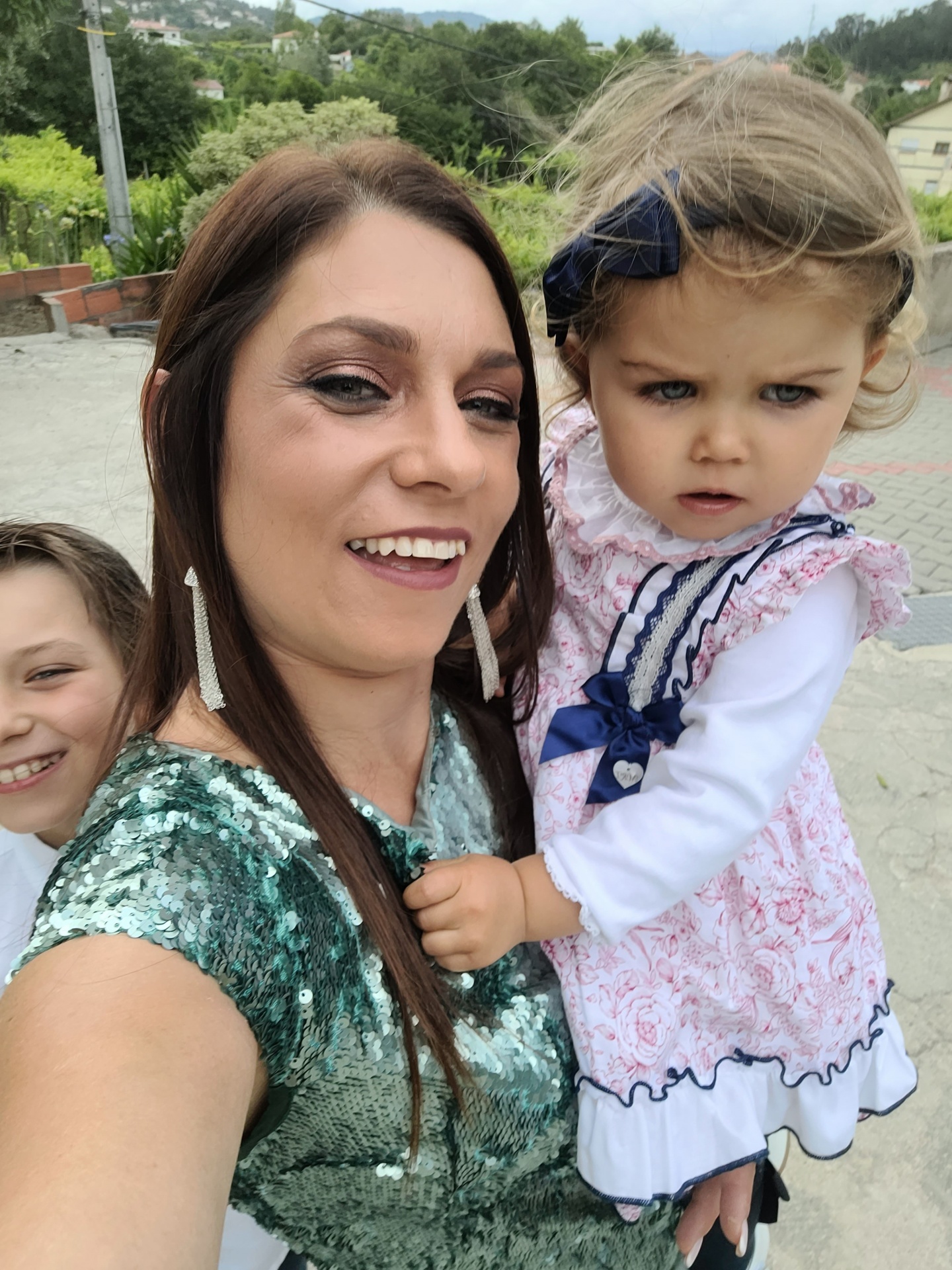 Mulher com vestido verde brilhante segurando criança com vestido rosa e branco ao ar livre