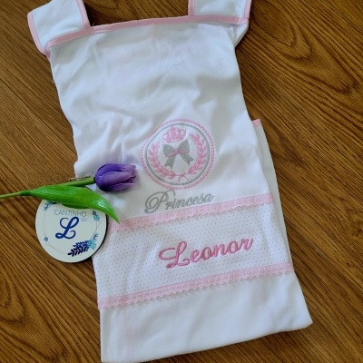 Tecido branco com bordado rosa e etiqueta redonda sobre superfície de madeira