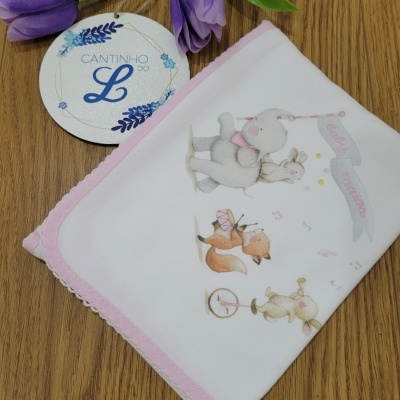 Fralda branca com desenhos de animais e texto Baby Moon ao lado de flores roxas e etiqueta circular em madeira