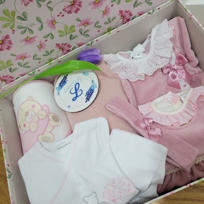 Caixa decorativa com roupas de bebé rosa e branco e copo de desenho de coelho.