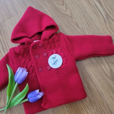 Casaco de malha vermelho com capuz e botões numa superfície em madeira clara com flores roxas ao lado