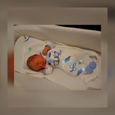 Bebé recém-nascido a dormir vestido com pijama branco e azul numa cama branca.