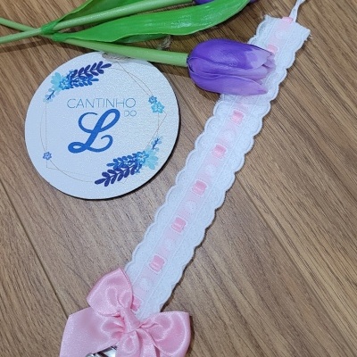 Fita de chupeta branca e rosa com laço e ursinho, tulipas roxas artificiais e um cartão redondo em fundo de madeira