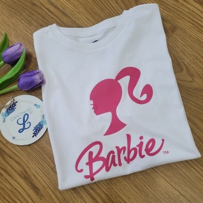 T-shirt branca com estampa rosa Barbie sobre madeira, com tulipas e etiqueta ao lado