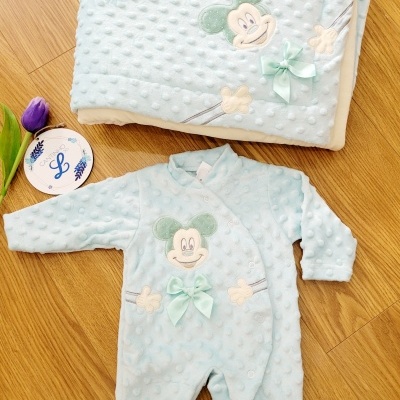Conjunto de pijama e manta azul claro para bebé com textura de bolinhas e decoração de rato e laço em fundo de madeira