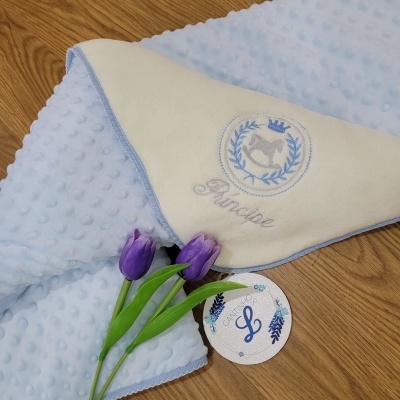 Manta azul claro texturizada com capa branca bordada e tulipas roxas