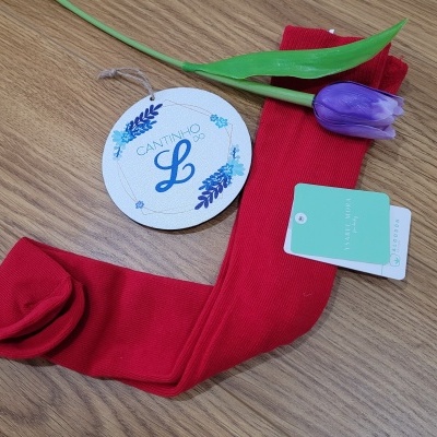 Meias vermelhas, etiqueta verde e branca, flor artificial roxa e etiqueta redonda branca sobre madeira