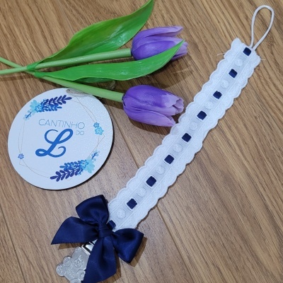 fita branca com laço azul escuro, flores roxas e cartão redondo com texto CANTINHO DO L