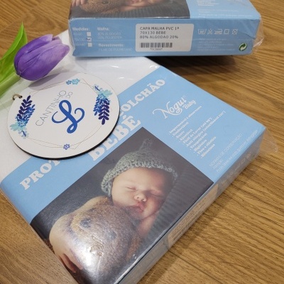 Embalagens azuis de protetores de colchão para bebé com imagem de bebé a dormir e informações do produto.