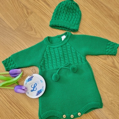 Macacão e gorro de bebé verdes em malha com textura frisada, botões de madeira, tulipas roxas e prato branco com inscrições azuis