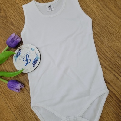 Body branco para bebé com botão de pressão, flores roxas e cartão decorativo num fundo de madeira.