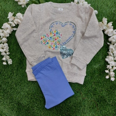 Conjunto infantil com sweatshirt cinza claro decorada com corações coloridos e calças azul claro sobre relva e flores brancas