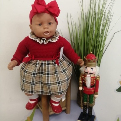 Boneca com roupa vermelha e saia xadrez sentada em cadeira com soldado decorativo ao lado e plantas verdes
