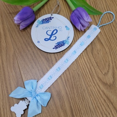 Prendedor de chucha branco com laço azul e ursinho, flores roxas e placa com texto
