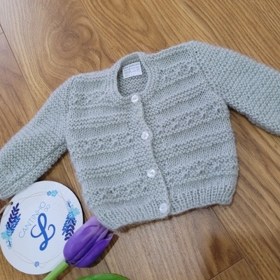 casaco de malha cinzenta com botões brancos e padrão texturizado sobre chão de madeira claro